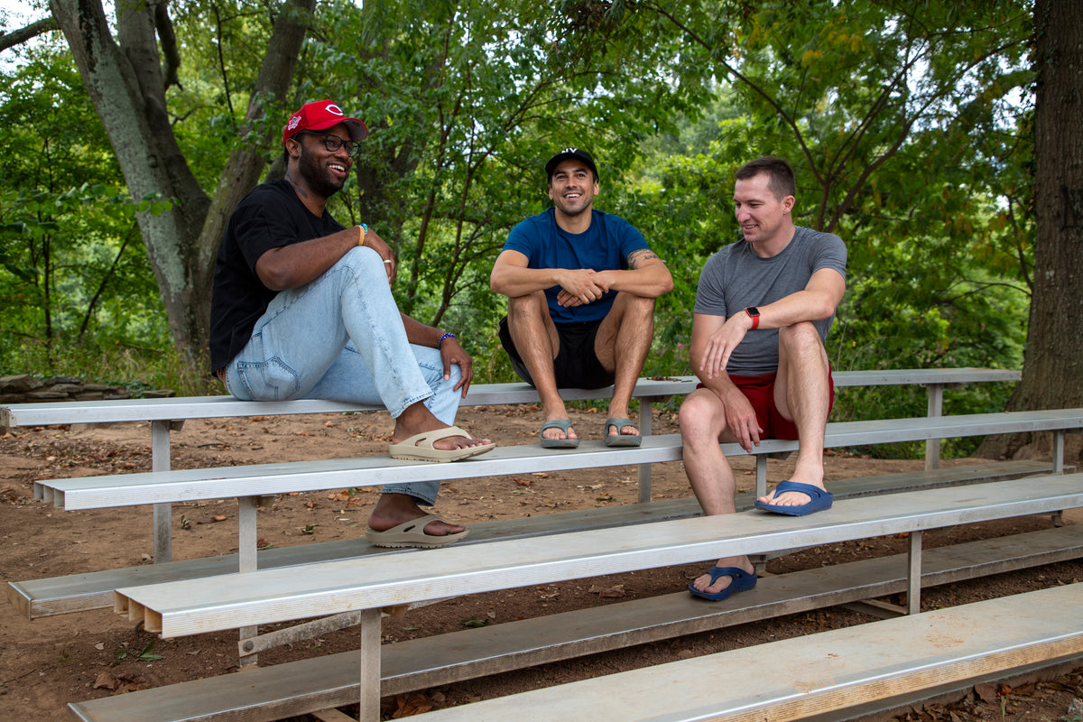 Friends relaxing on bleachers wearing Oka Recovery flip flops
